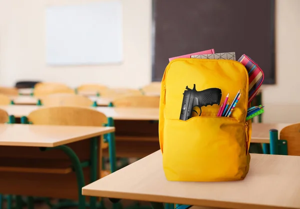 School shooting. Backpack with gun and stationery in classroom