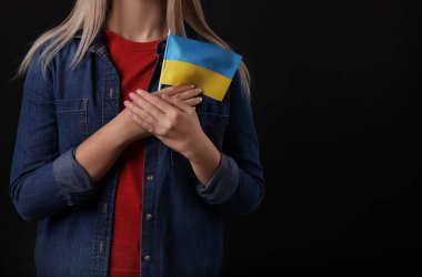 Woman holding Ukrainian flag on black background, closeup. Space for text