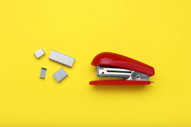 New bright stapler with staples on yellow background, fat lay. School stationery