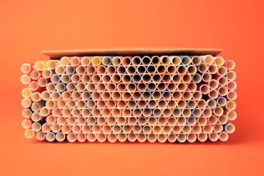 Box with many paper drinking straws on orange background