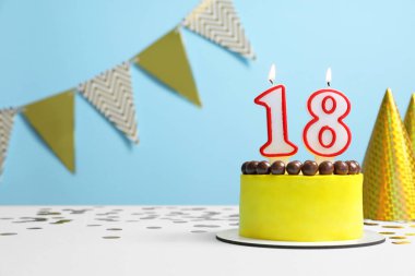 Coming of age party - 18th birthday. Delicious cake with number shaped candles on light blue background, space for text