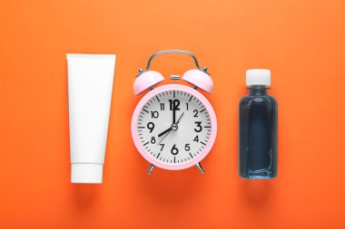 Container with toothpaste, alarm clock and bottle of mouthwash on orange background, flat lay