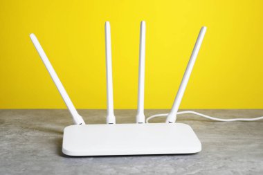 New white Wi-Fi router on grey textured table against yellow background