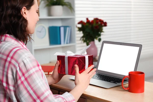 Valentine\'s day celebration in long distance relationship. Woman holding gift box while having video chat with her boyfriend via laptop indoors, closeup