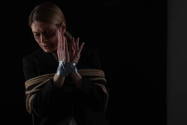 Scared woman tied up and taken hostage on dark background. Space for text