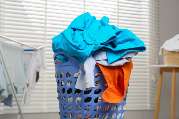 Plastic laundry basket overfilled with clothes indoors