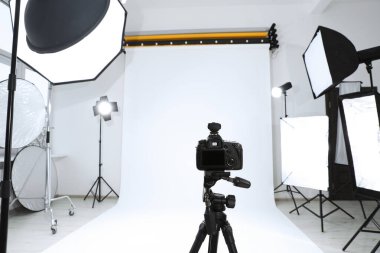 Tripod with camera and professional lighting equipment in modern photo studio