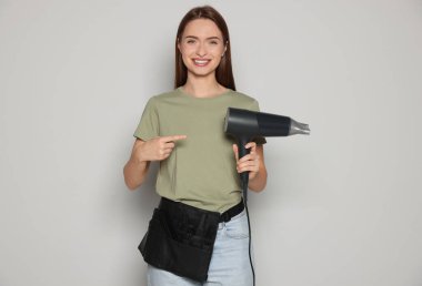 Portrait of happy hairdresser with hairdryer on light background