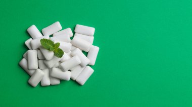 Tasty chewing gums and fresh mint leaves on green background, flat lay. Space for text