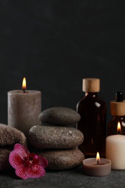 Beautiful composition with burning candles, spa stones and different care products on dark grey table