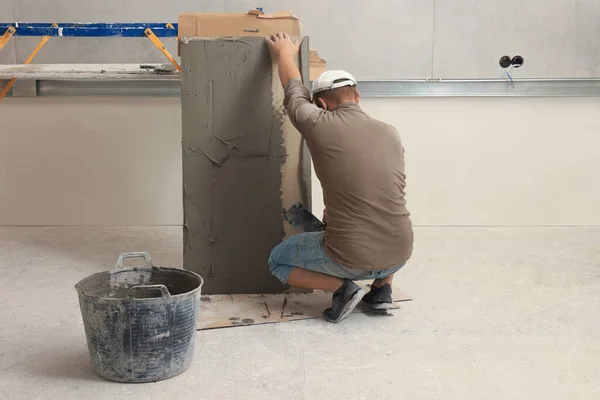Worker spreading adhesive mix over tile with spatula