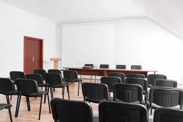 Empty conference room with projection screen, wooden table and many chairs
