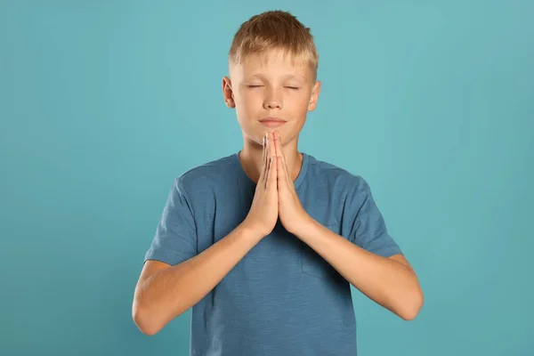 Boy with clasped hands praying on turquoise background