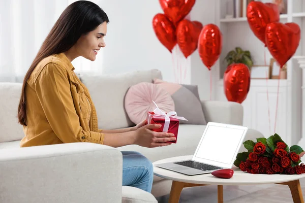 Valentine\'s day celebration in long distance relationship. Woman holding gift box while having video chat with her boyfriend via laptop at home