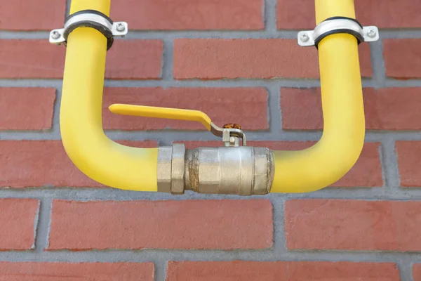 Yellow gas pipe on red brick wall outdoors, closeup