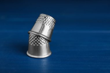 Silver thimbles on blue wooden table, space for text. Sewing accessories