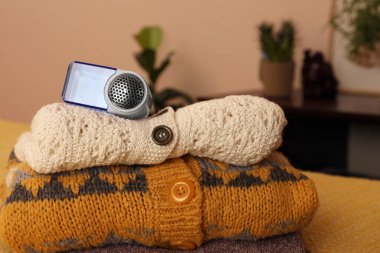 Modern fabric shaver and knitted clothes on orange blanket indoors, closeup