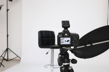 Camera on tripod, bar stool and professional lighting equipment in modern photo studio, space for text