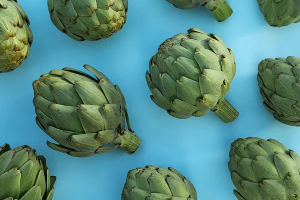 Whole fresh raw artichokes on light blue background, flat lay