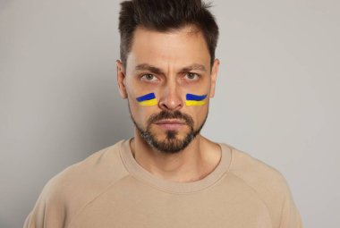 Angry man with drawings of Ukrainian flag on face against light grey background