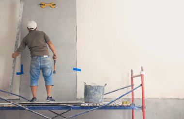 Worker installing tile on wall indoors, back view