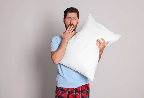 Tired man with pillow yawns on light grey background