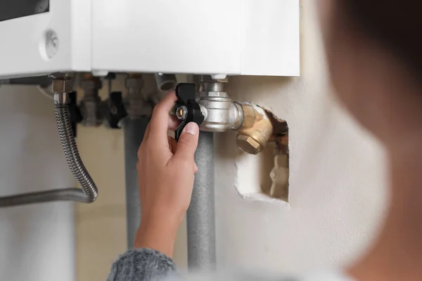 Woman turning on valve of gas boiler indoors, closeup
