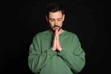 Elleri sıkıca bağlı siyah arka planda dua eden adam.