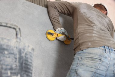 Worker installing wall tile with vacuum holder indoors, closeup