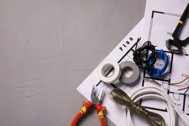 Different wires, electrician's tools and schemes on grey table, flat lay. Space for text