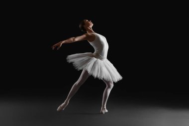 Young ballerina practicing dance moves on black background