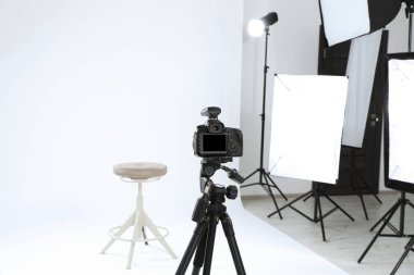 Tripod with camera, bar stool and professional lighting equipment in modern photo studio