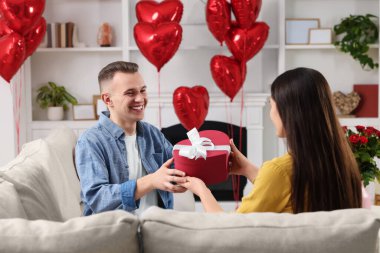 Man receiving gift box from his girlfriend at home. Valentine's day celebration