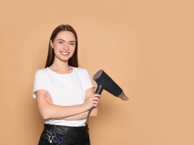 Portrait of happy hairdresser with hairdryer on beige background. Space for text