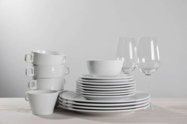Set of clean dishware and glasses on white wooden table against light background