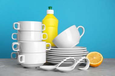 Clean tableware, dish detergent and lemon on grey table against light blue background