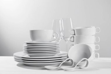 Set of clean dishware and glasses on white wooden table against light background