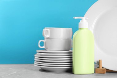 Set of clean tableware and dish detergent on grey table against light blue background. Space for text