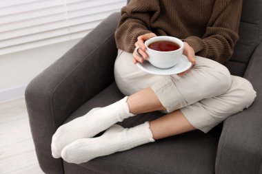 Woman in warm socks relaxing with cup of tea at home, closeup. Space for text