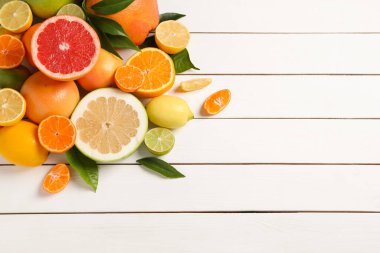 Different citrus fruits with fresh leaves on white wooden table, flat lay. Space for text