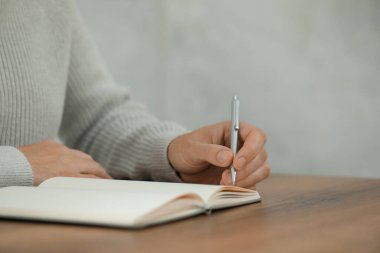 Man writing in notebook at wooden table, closeup