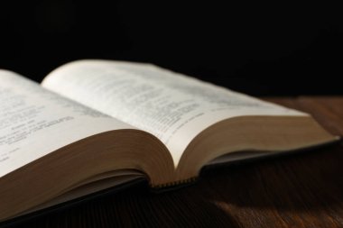 Open Bible on wooden table against black background, closeup