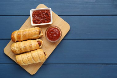 Delicious sausage rolls and ketchup on blue wooden table, top view. Space for text