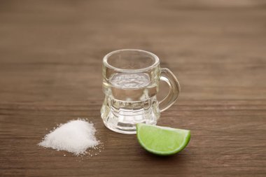 Mexican tequila shot with lime slice and salt on wooden table, closeup. Drink made from agave