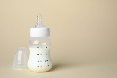 Feeding bottle with infant formula on beige background. Space for text