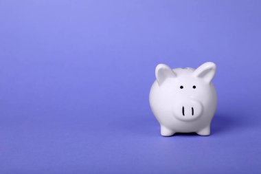 Ceramic piggy bank on purple background, space for text. Financial savings
