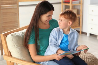 Mother reading book with her son on armchair in living room at home