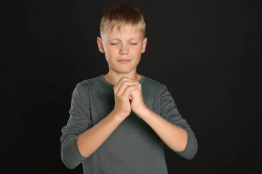 Boy with clasped hands praying on black background