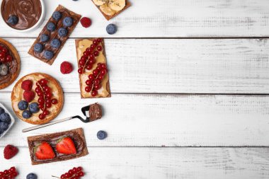 Fresh rye crispbreads and rusks with different toppings on white wooden table, flat lay. Space for text