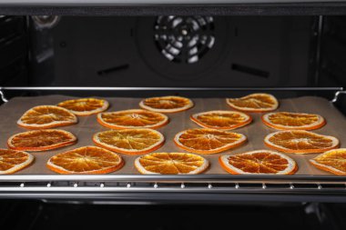 Many dry orange slices on parchment paper in oven